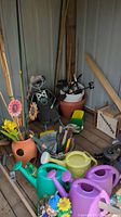 Overview of garden supplies including bamboo stakes, pots, metal ornaments, small tools, plastic watering cans and artificial flowers