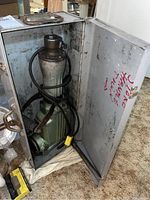 Open metal case showing green and silver Hitachi hammer drill inside with power cord coiled inside the case.