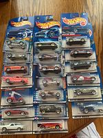 Photo shows 20 sealed Hot Wheels cars in original packaging, arranged flat on a wooden surface. Various car models and designs visible.