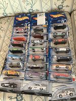 Full view of 24 Hot Wheels cars in original packaging arranged in three columns on sofa.