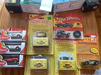 Overview of lot including three Coca-Cola branded Hot Wheels cars in white with original packaging, four Matchbox Originals vehicles in yellow blister packs, and a black police vehicle Hot Wheels car.