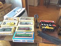 Overview photo showing multiple HO scale model train cars in Life Like packaging, a Tyco Santa Fe engine, and some loose engines and accessories on a wooden table.