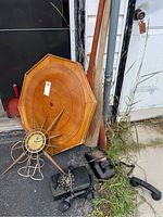 Photo showing the Crokinole board with crokinole discs, two wooden paddles, vintage clock, wooden bat, and rotary phones arranged on the ground outside against a white door and black refrigerator.
