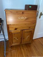 Front view of pine secretary desk showing drop down front, middle drawer, and two lower doors with wood decals and knobs.