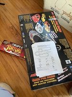 Top view of ARTN Grand Prix Racing box with four racing cars pictured and a printed instruction sheet placed on top, plus a smaller unopened box labeled Triple Torture nearby.