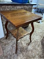 Front angle view showing the square oak top, carved rim detail, cabriole legs, and lower scalloped shelf, set on a beige carpet.