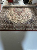 Photo showing Persian style rug partially rolled up with cream background and detailed floral medallion pattern.
