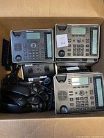 Photo showing several AudioCodes 440HD IP phones stacked in a box, including handsets and cords visible.