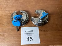 Two round silver disc padlocks placed on a wooden surface with blue keys inserted in each one.
