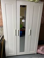 Front view of a white 3 door wardrobe with a full-length mirror on the middle door, closed.