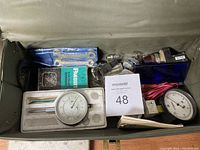 Box with wrenches, thermometer, round gauges, light bulbs, electrical components, and test leads.