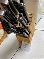 Photo of wooden knife block with multiple knives of varying sizes with black handles.
