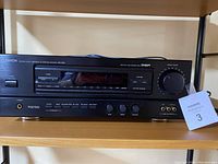 Full frontal photo of Denon AVR-2000 receiver showing power switch, tuning buttons, and volume knob on wooden shelf.