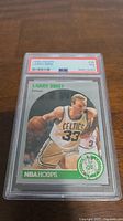 Front of the 1990 Larry Bird NBA Hoops basketball card graded PSA 7, showing Larry Bird in Celtics uniform dribbling the ball.