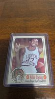 Front view of 1992 Kobe Bryant Lower Merion High School basketball card in plastic sleeve, showing Kobe smiling and holding basketball, making a peace sign.
