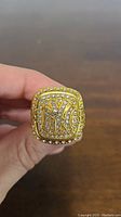 Front view of replica ring top showing New York Yankees 'NY' logo with clear stones around and on the logo on a gold-tone metal ring.