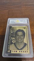 Front of the 2003 Tom Brady 23kt Gold football card graded Gem Mint 10 by WCG, showing black and gold printed portrait of Tom Brady with New England Patriots text.