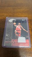 Photo of Lebron James rookie basketball card in protective plastic case on wooden surface.