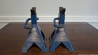 Pair of blue axle stands with a triangular base, showing front view with labels and side handles.