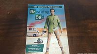 Front cover of Breaking Bad Complete First Season DVD set showing main character Walter White with gun in desert setting.