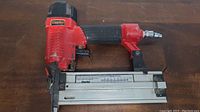 Side view of Clarke red and black pneumatic brad nailer showing trigger, handle, and nail magazine.