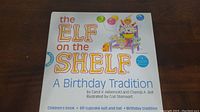 Front cover of children's book titled 'The Elf On The Shelf: A Birthday Tradition' with colorful text and birthday-themed illustrations.