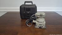 Porter Cable electric finishing sander in front of the carrying case on a wooden surface.