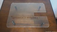 Top view of the clear acrylic Sew Steady portable table on a wooden surface, showing four adjustable legs and rectangular sewing machine offset cutout.