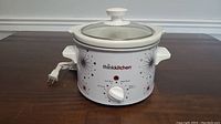 Front view of the small white Thinkkitchen crock pot slow cooker showing decorative starburst patterns and attached power cord.