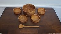 Wooden salad bowl set arranged on table with large bowl, four smaller bowls, and serving spoon visible.