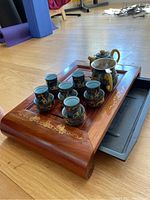 Overall view of the tea set displayed on the wooden tray showing the teapot, pitcher, eight cups, and the pull-out drawer reservoir beneath the tray.