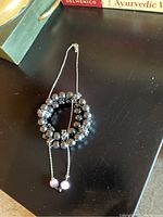 Black onyx beaded bracelet coiled with silver necklace displaying three rhinestone beads, two pale pink, one black, positioned on dark surface.