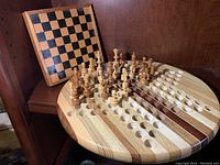 Wooden chess board with chess pieces set up alongside a round wooden Chinese checker board with colored marbles positioned in the holes.