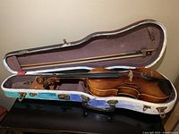Violin in open case showing violin and bow inside burgundy fabric lining