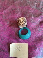 Photo of two chunky rings on purple fabric: one sterling silver Tibetan detailed ring and one turquoise glass-colored ring.