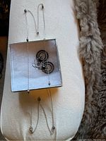 Photo showing silver-tone necklace laid out alongside a pair of black and silver circular earrings placed on a small box.