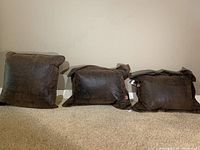 Three pillows shown with leather-like material side visible, dark brown color, smooth texture.
