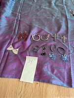 Photo showing all earrings and ring laid out on purple fabric, displaying 6 pairs of earrings and one ring.