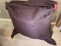 Brown Fatboy bean bag chair made of heavy duty canvas fabric, lying against a wall showing shape and material.