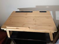 Front view of bamboo folding tray table with black device holder slots and wooden lip on front edge