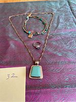 Photo showing larimar pendant necklace, turquoise bracelet, and purple stone pinkie ring on patterned fabric