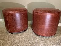 Pairs of circular red leather ottomans with visible wear and small scuffs, viewed from front and side angles.
