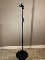Full view of the black adjustable microphone stand showing the round heavy base and microphone clip on top.