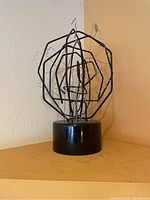 Abstract metal wire sculpture shaped into faces and hands on black base.