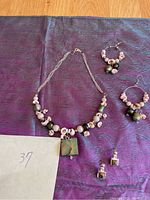 Photo of green and white sea shell bead necklace with square pendant and two pairs of earrings on purple fabric background.