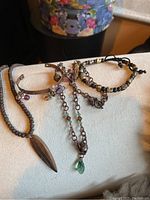 Photo of four skeleton themed jewelry pieces including two bracelets, one necklace with wooden leaf pendant and a copper skull cuff bracelet.