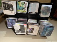 Photo of DVDs and CDs laid out on a black surface, showing multiple stacks of DVDs in cases and paper sleeves with various cover art.