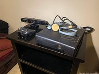 Side angle view of Xbox 360 console with Kinect sensor bar, wireless controller, and wired headset on black table.