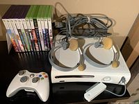Xbox 360 console with controller, remote, two headsets, power cables, and games.