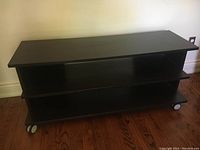 Front view of the large dark wood TV table with two shelves and caster wheels on wood floor.